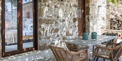 a table and chairs on a patio with a stone wall at Stairs Homes & Suites in Kamária