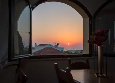 a table with a vase of flowers and a sunset through a window at Skandalis Apartments with pool in Chorafakia