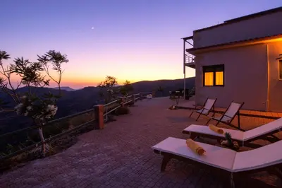 a house with a balcony with chairs and a sunset at Best View Mountain Villa in Teménia
