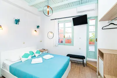 a white bedroom with a blue bed and a tv at Alegria Pension in Chania Town