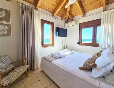 a bedroom with a bed and a chair and windows at Seastar seafront villa in Kalamaki Chanion