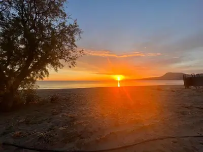 a sunset on a beach with a bench and the ocean at Blue Green Villa Kalyves eco pool premium quality in Kalyves