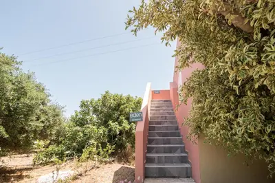 a staircase leading up to a pink building with trees at eden of grameno in Palaiochóra