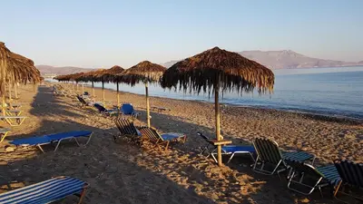 a beach with chairs and straw umbrellas and the ocean at Camping Mithimna in Kissamos
