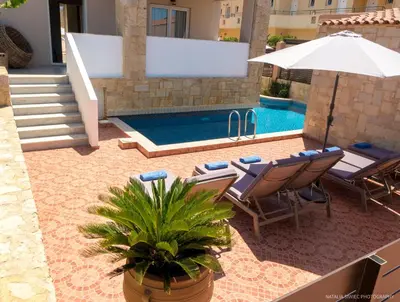 a pool with chairs and an umbrella next to a house at Alexandra SeaSide Villas in Plataniás
