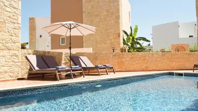 a swimming pool with two lounge chairs and an umbrella at Alexandra SeaSide Villas in Plataniás