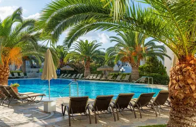 a swimming pool with chairs and palm trees at Castle Suites Hotel in Plataniás