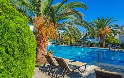 a swimming pool with two chairs and palm trees at Castle Suites Hotel in Plataniás