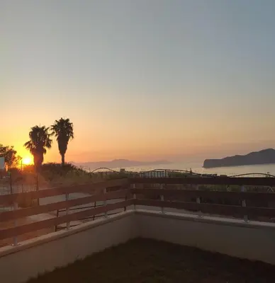 a sunset from the balcony of a house with palm trees at Wish Sea & Mountain View in Stalos