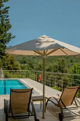 a patio with two chairs and an umbrella next to a pool at Villa Kalamitsi Luxury Villa in Apokorona Chania in Kariá