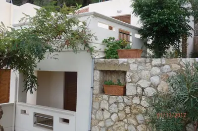 a white house with plants on a stone wall at Ravdoucha Beach Studios in Ravdhoúkha