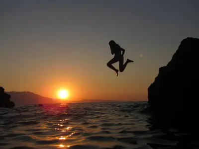 a person jumping off a cliff into the water at sunset at Ravdoucha Beach Studios in Ravdhoúkha