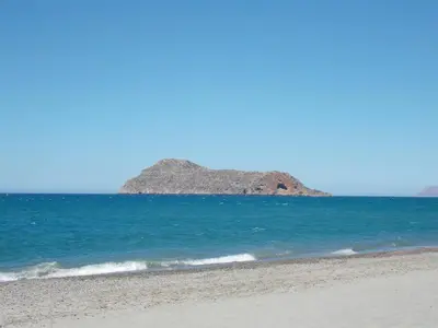 a beach with a rocky island in the ocean at Lissos Beach in Plataniás