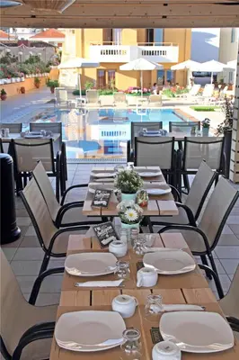 a restaurant with tables and chairs next to a pool at Esperides Beach Hotel Apartments in Stalos
