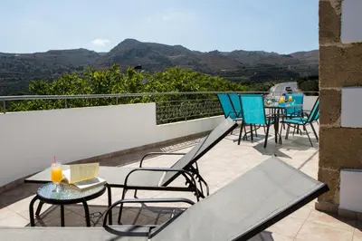 a balcony with chairs and tables with mountains in the background at Basilikos traditional house, 10' from Falasarna in Kissamos