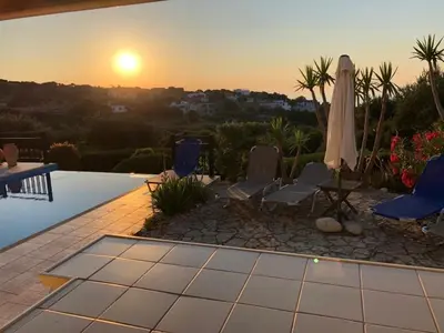 a sunset over a patio with chairs and an umbrella at Villa Ravdoucha Homeleader in Ravdhoúkha