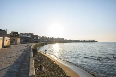 a beach with people sitting on the sand and the water at Just For Two in Chania Town
