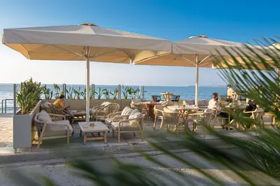 people sitting at tables under an umbrella on the beach at Just For Two in Chania Town