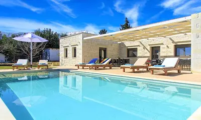 a swimming pool with chairs and an umbrella next to a house at Orientem Villa Heated Pool in Georgioupoli