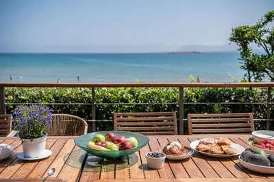 a wooden table with plates of food and the beach at The House By The Sea in Kato Daratso