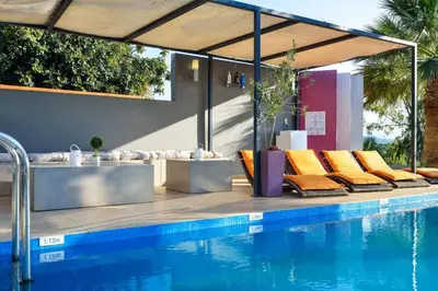 a pool with orange lounge chairs next to a swimming pool at Adorno Luxury Villa in Chorafakia