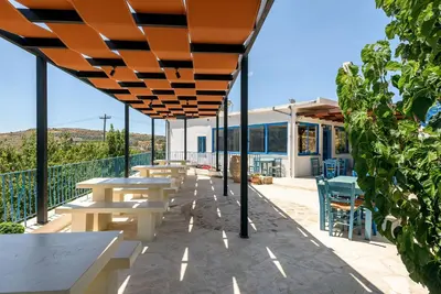 a patio with tables and chairs under an orange umbrella at Minos Country Living Apartments in Agrilés