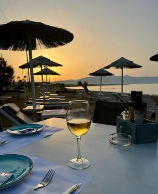 a glass of wine sitting on a table with a view of the beach at Wave rooms in Maleme