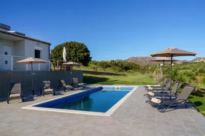 a pool with chairs and umbrellas next to a house at RODOU Suites & Villas in Chania Town