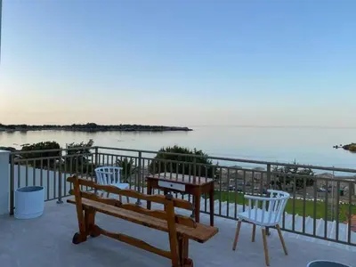 a bench and two chairs on a balcony overlooking the water at Houmas Apartments in Yialós