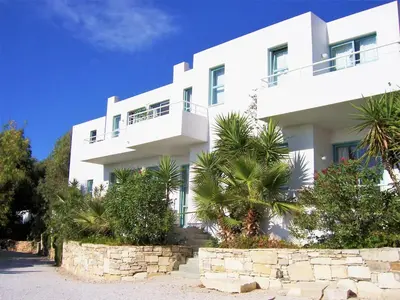 a white building with palm trees in front of it at Hotel Plakures in Falasarna