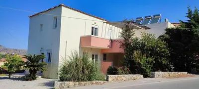 a white and pink house with bushes and trees at Kalyves Mili's house sea view in Plaka