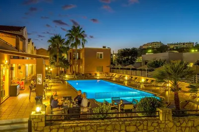 a group of people sitting around a pool at night at Theos Holidays Apartments in Kato Daratso
