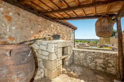 a building with a stone wall with a large bucket at Traditional Cretan Villa George - Private Pool in Kambánion
