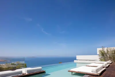 a pool with lounge chairs and the ocean in the background at Cavo Dago in Chania Town