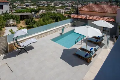 a swimming pool with two umbrellas and two lounge chairs at Lilium Stone Villa in Varípetron