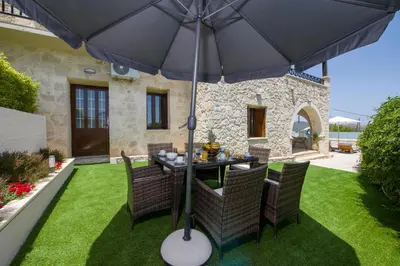a table and chairs under an umbrella on a lawn at Lilium Stone Villa in Varípetron