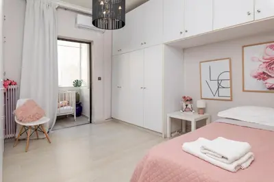 a white bedroom with a pink bed and a chair at Chania dream apartment in Chania Town