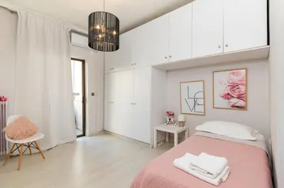 a white bedroom with a pink bed and a chair at Chania dream apartment in Chania Town
