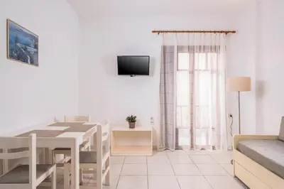 a white living room with a table and a tv at Captain Michalis Apartments - 750m from Kalamaki Beach in Galatás