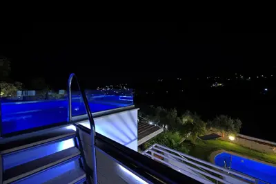 a balcony with a view of a city at night at Villa Eftychia - villa with 2 private pools!!! by PosarelliVillas in Almirida