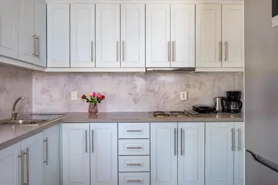 a white kitchen with white cabinets and a vase of flowers at Plori - Molos Apartments in Loutro