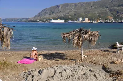 a woman sitting on a beach next to the water at Thyme Sea View Apartments by 8essentially in Souda