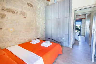 a bedroom with an orange and white bed and a stone wall at SpiliaInn in Spiliá