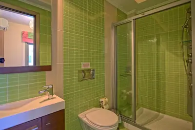a green tiled bathroom with a toilet and a shower at Cabanavillas Rio by PosarelliVillas in Agia Marina Nea Kydonias