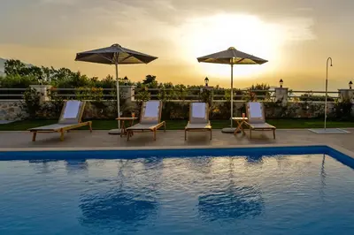 a pool with chairs and umbrellas on a patio at Villa Despanto by PosarelliVillas in Litsárdha
