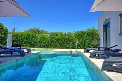 a swimming pool with chairs and an umbrella at Villa Zaneti by PosarelliVillas in Agia Marina Nea Kydonias