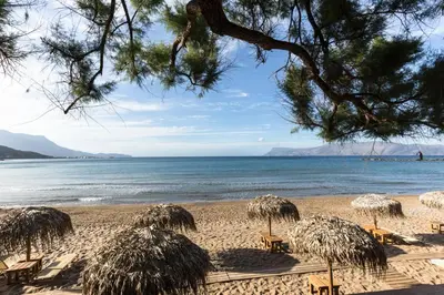 a beach with chairs and straw umbrellas and the ocean at Armonia in Kissamos