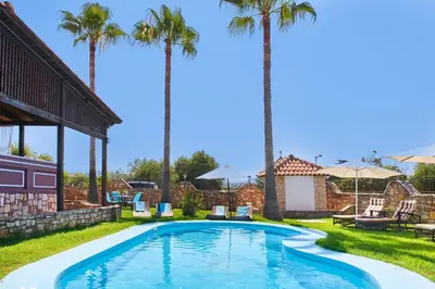 a swimming pool with palm trees in a yard at Villa Milon by PosarelliVillas in Skinés