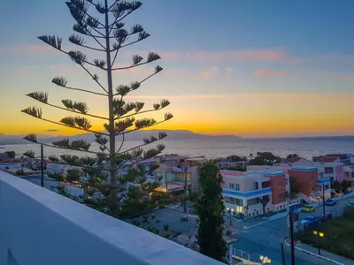 a view of a city at sunset with a pine tree at Giannis & Maria Gramvousaki Apts in Agia Marina Nea Kydonias