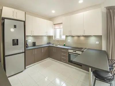 a kitchen with white cabinets and a table and a refrigerator at Fully renovated apartment in the city centre with roof garden! 3 minutes from the bus station and 6 minutes from the old town in Chania Town